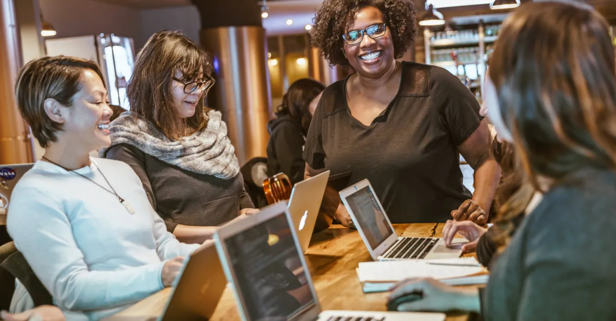 Smiling people at an office table working on laptops