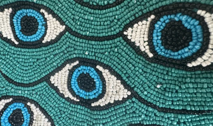 Beaded pattern of blue eyes on a teal background.