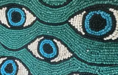 Beaded pattern of blue eyes on a teal background.