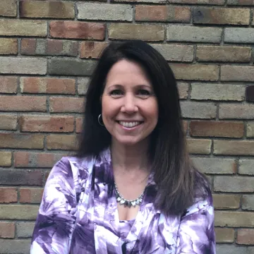 Lori smiling in front of a brick wall