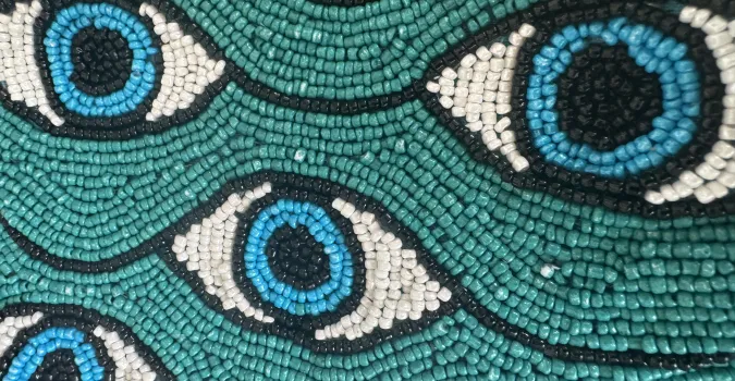 Beaded pattern of blue eyes on a teal background.