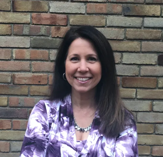 Lori smiling in front of a brick wall